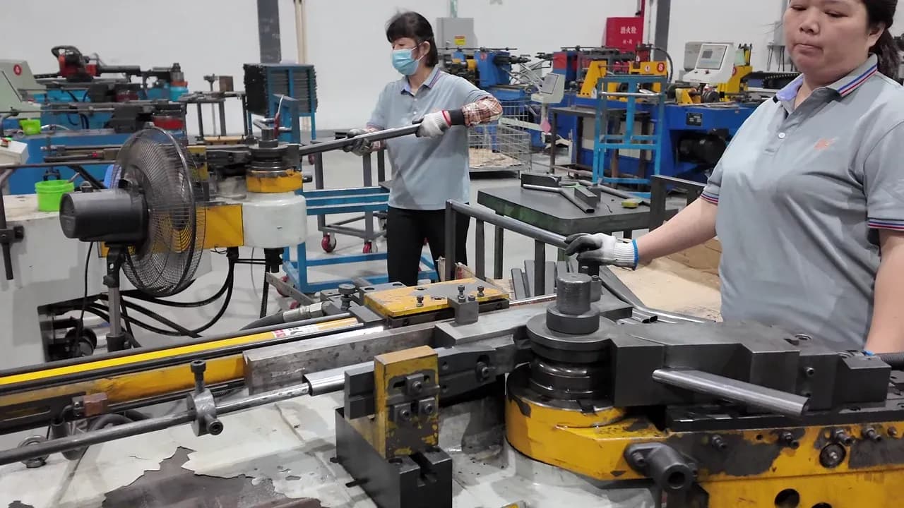 Zwei Yuzhen Furniture-Mitarbeiter führen Metallrohre an benachbarten Biegestationen