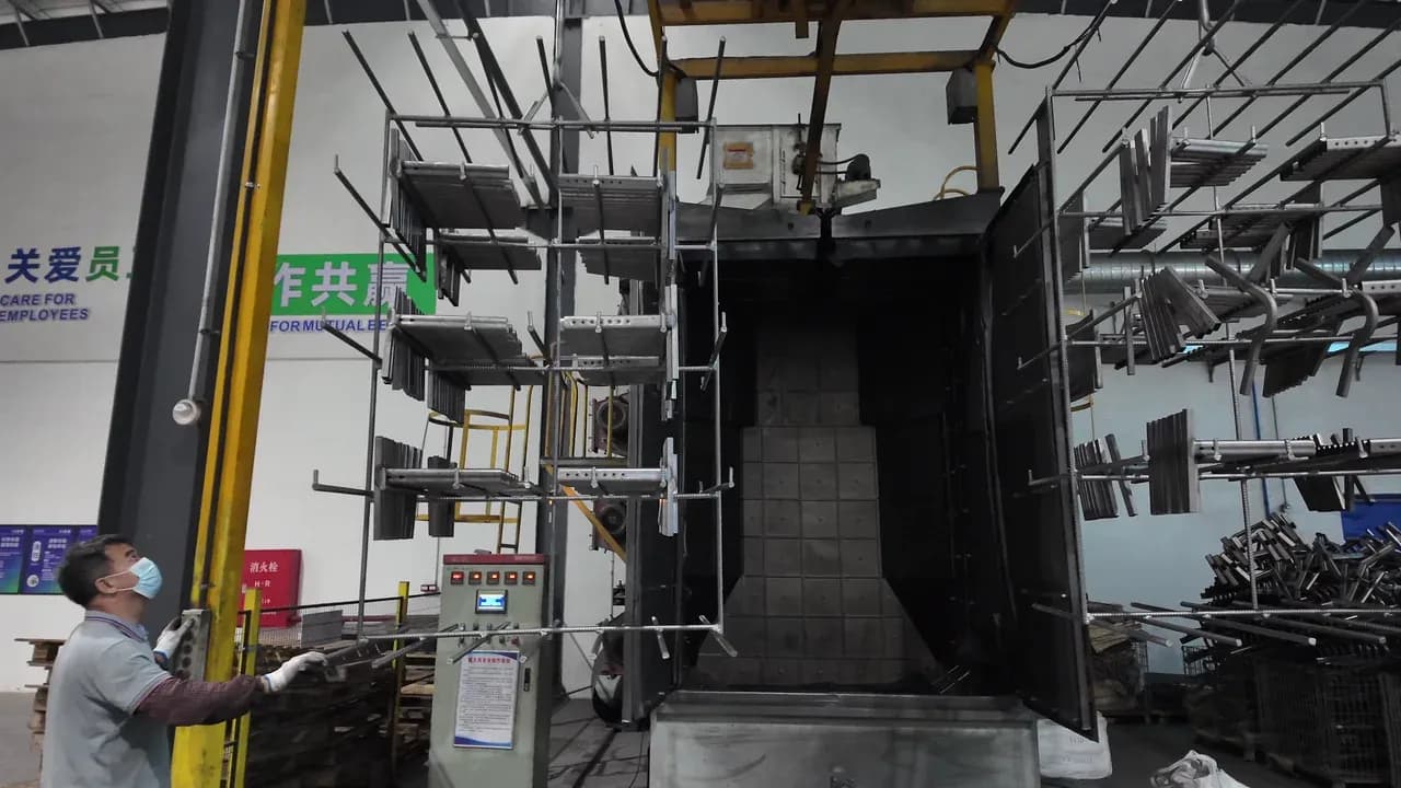 steel surface preparation Worker guiding suspended steel components toward a sealed high-temperature treatment chamber